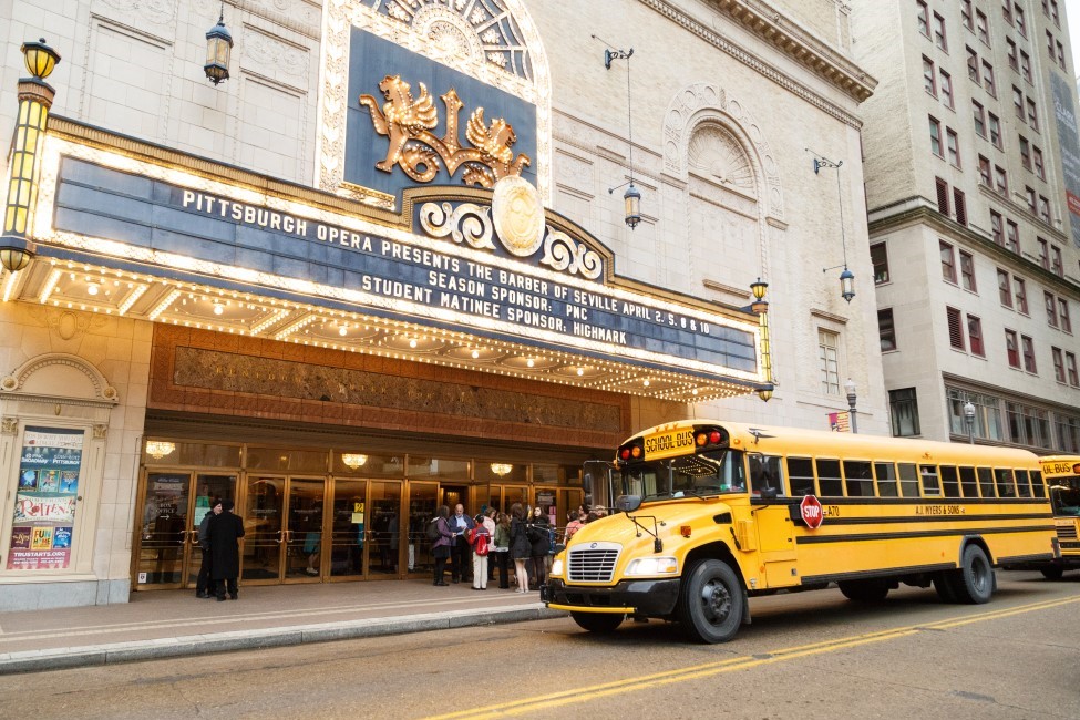 A yellow school bus pulls up under the Benedum Center marquee for a Pittsburgh Opera Barber of Seville student matinee