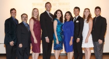Nine Pittsburgh Opera Resident Artists and staff in formal wear pose in a line before a warm-lit wall