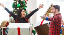 A soprano in black spreads her arms beside a man in plaid before a Christmas tree at Children's Hospital