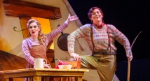 Gretel sings at a kitchen table as Hansel leans on a broom in Pittsburgh Opera's Hansel & Gretel