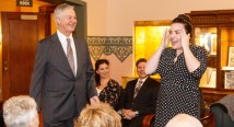 Christopher Hahn stands beside a young woman in black addressing a seated audience at a Meet the Artists reception
