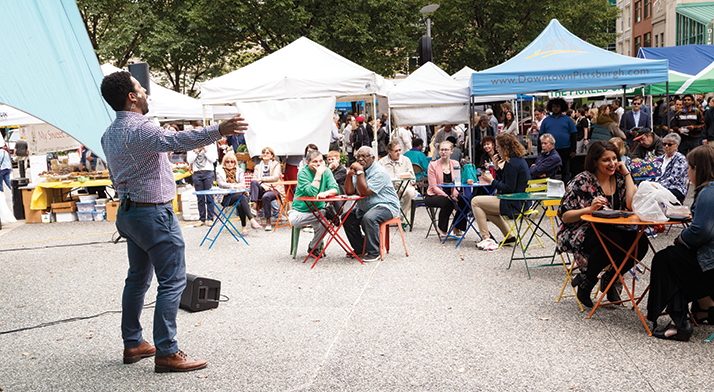 Resident Artist Ben Taylor sings with arms outstretched to a seated crowd at the Market Square farmers market