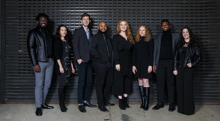 Pittsburgh Opera's 2021-22 Resident Artists all dressed in black or grey posing for a picture in front of a black wall