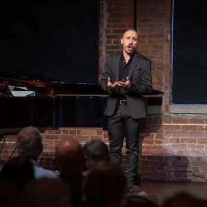 A singer performs beside a grand piano for a seated audience at a Pittsburgh Opera Rising Stars concert