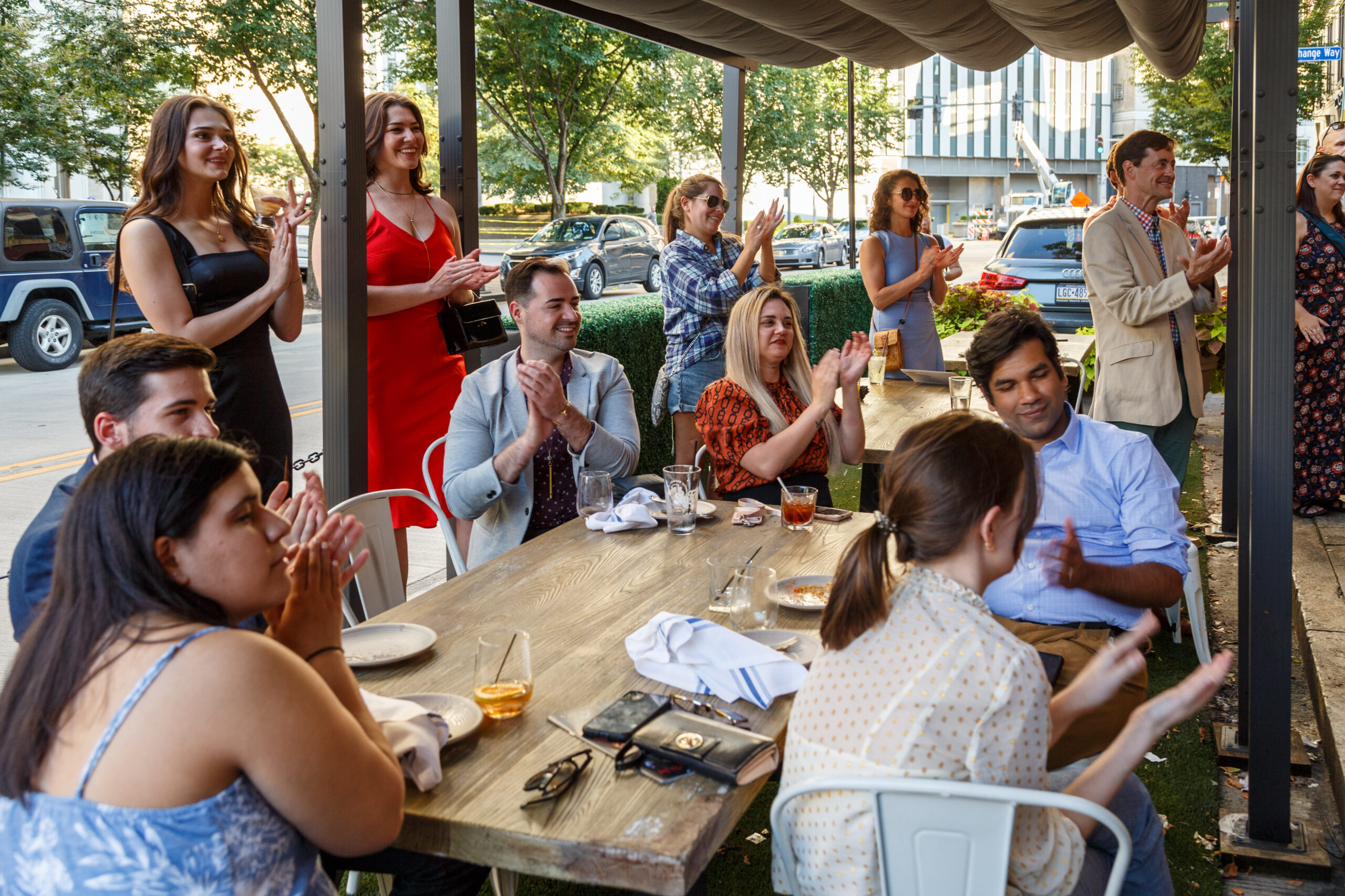 Guests applaud at long tables on a covered patio at the New Guard Summer Salon