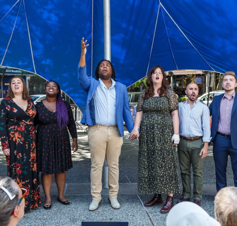 Pittsburgh Opera Resident Artists sing hand in hand under a blue canopy at the Market Square concert, downtown Pittsburgh
