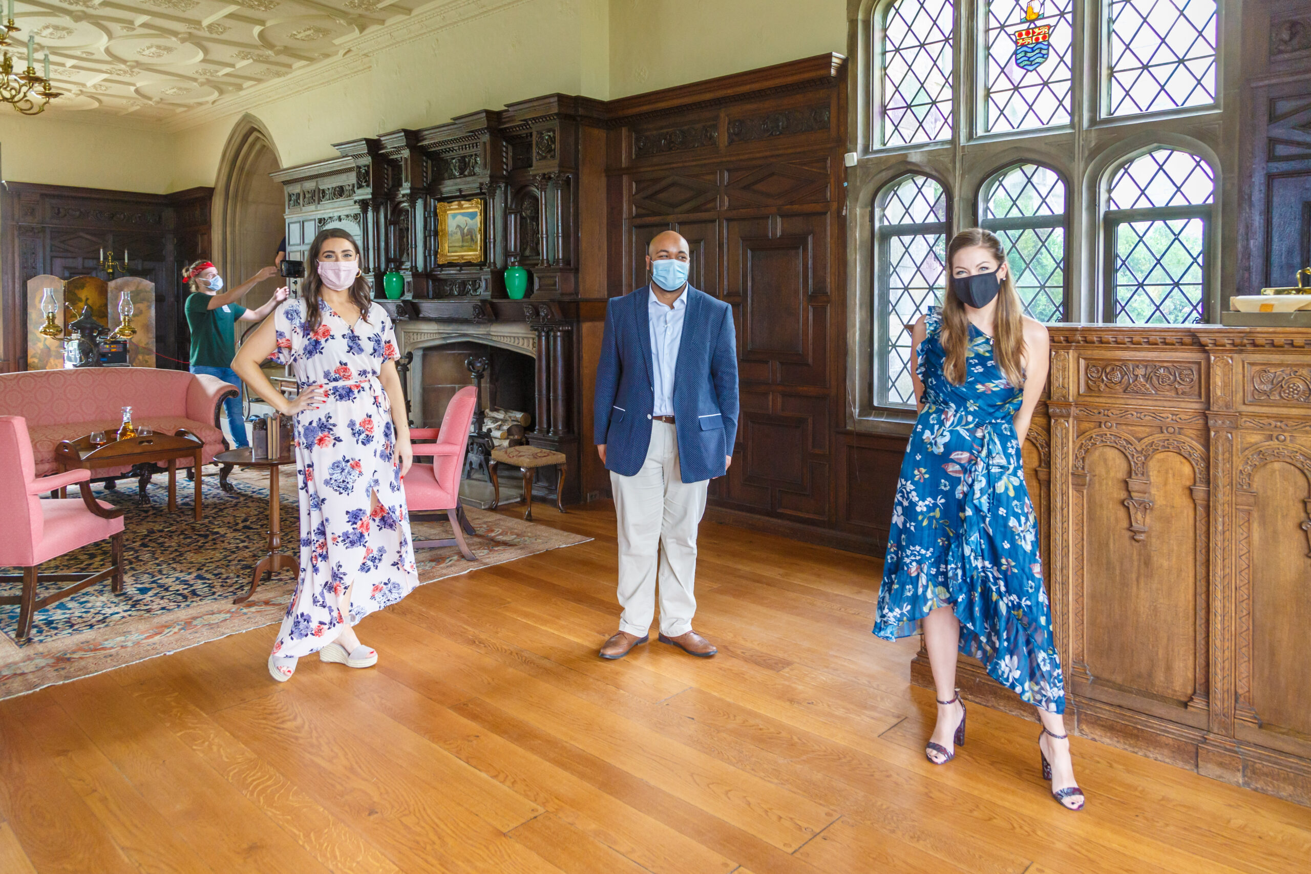 Three masked Resident Artists in summer dress pose in the wood-paneled great hall of Hartwood Acres mansion