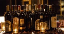 Rows of wine bottles glow behind candles at a Diamond Horseshoe Ball auction display