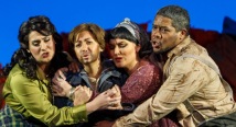 Four singers huddle together in refugee clothing before orange wreckage in Pittsburgh Opera's afterWARds
