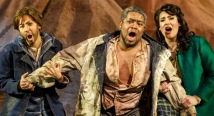 Idomeneo, wrapped in a blanket, stands between two young singers before orange wreckage in Pittsburgh Opera's afterWARds