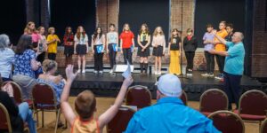 Bravo Academy summer campers line up on stage to take a bow as families applaud