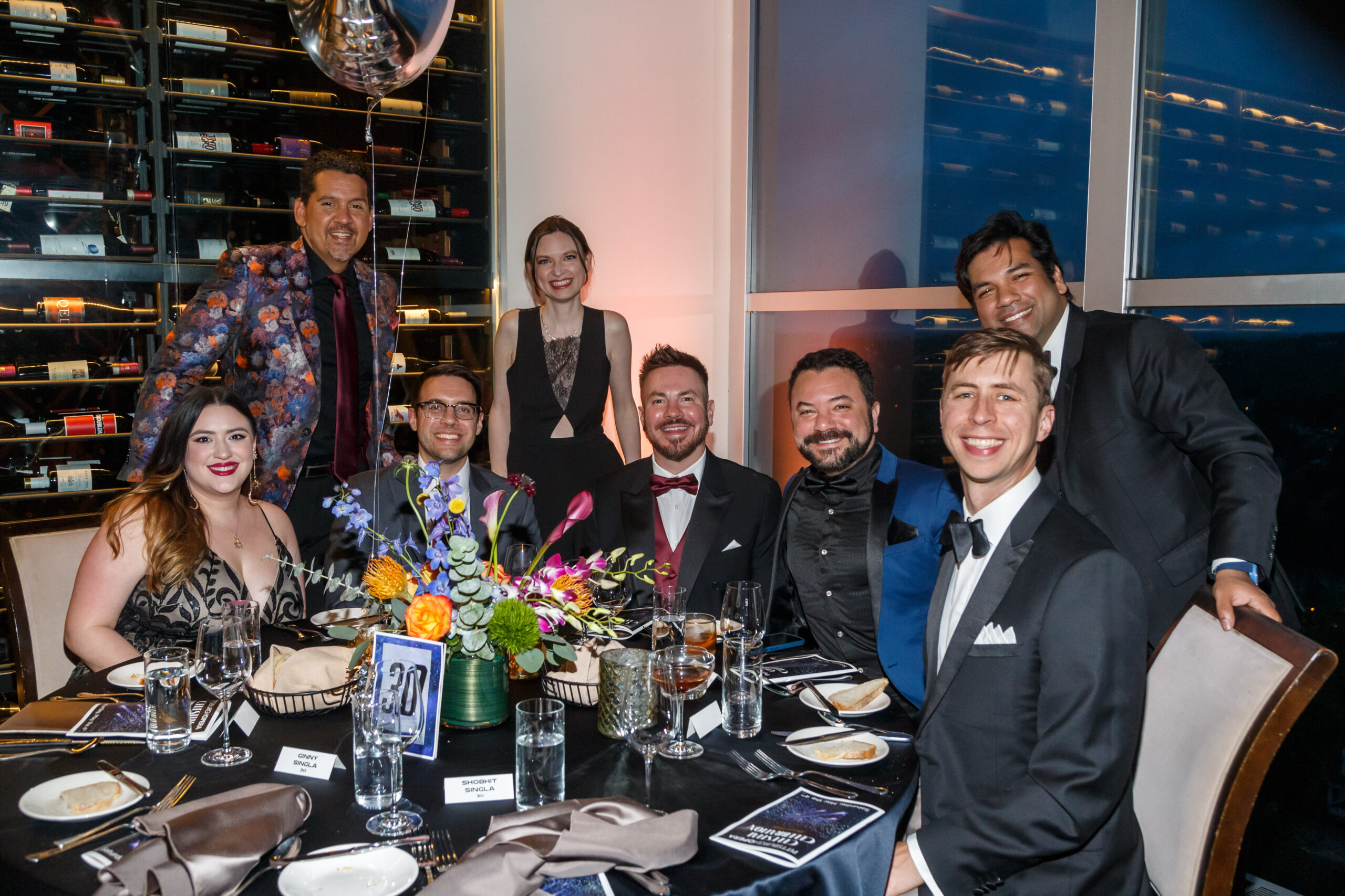 Seven guests in black tie pose around a flower-topped table at Maecenas XXXIX
