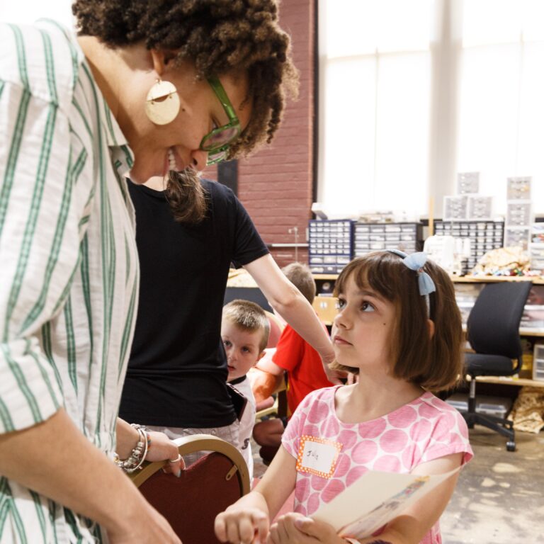 A volunteer bends to talk with a girl in a pink polka-dot shirt in the costume shop at Family Day 2024