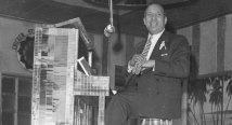 Vintage black and white shot: a smiling man in a suit at a glittering tiled piano under a hanging microphone