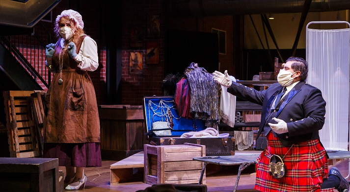 Angel Romero as Ferrando, in a kilt, gestures toward the masked Despina across a trunk of costumes in Cosi fan tutte, 2020