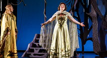 Ginevra in a white and gold gown spreads her arms before a blue backdrop in Pittsburgh Opera's Ariodante