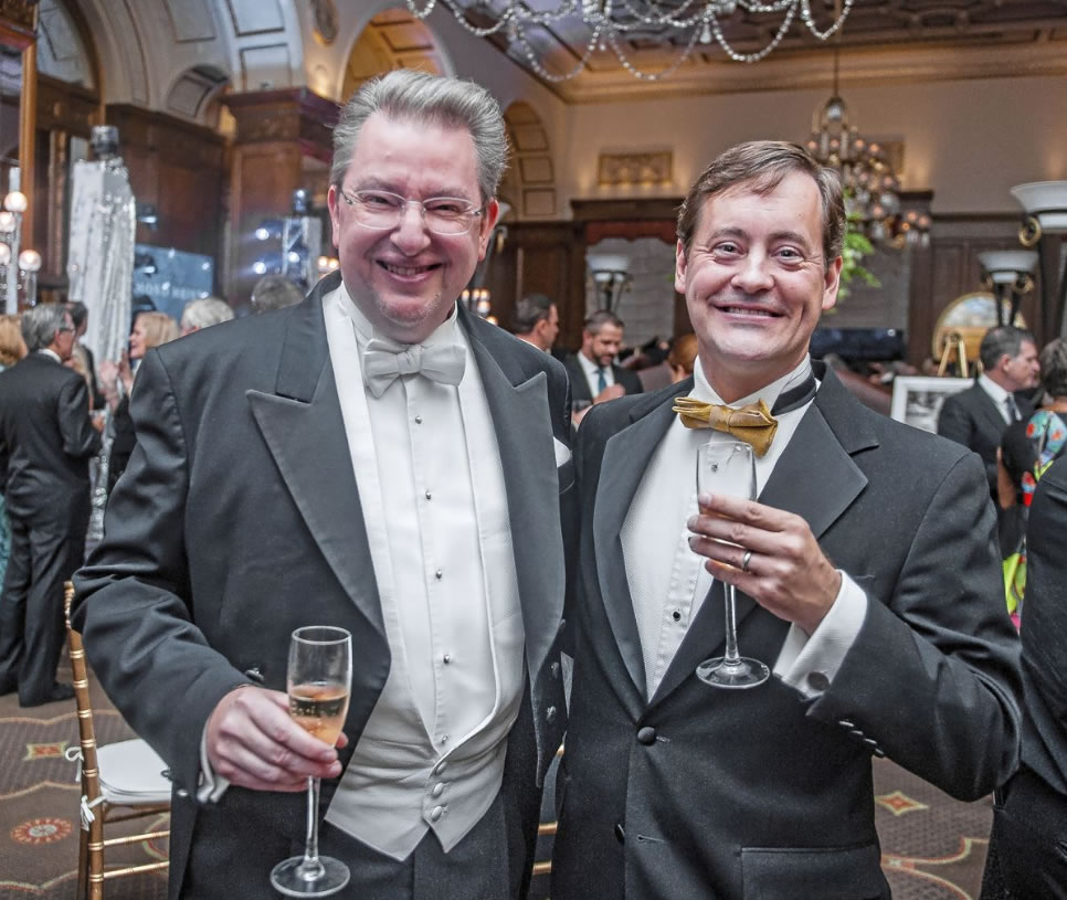 Two men in tuxes pose for a picture while holding glasses of alcohol