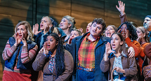 A crowd of townspeople in coats sing with hands cupped to their mouths in Pittsburgh Opera's The Flying Dutchman