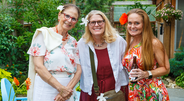 Three smiling women with flowers in their hair at a Friends of Pittsburgh Opera garden party