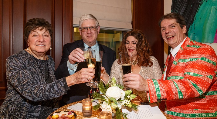 Four guests in holiday attire raise champagne glasses at a FRIENDS of Pittsburgh Opera holiday party