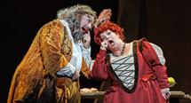 Falstaff, in a brocade coat and wild hair, leans toward a woman in a red gown in Pittsburgh Opera's Falstaff