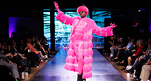 A model in a hot pink faux-fur coat raises an arm on the runway at Pittsburgh Opera's fashion show