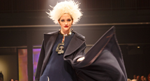 A model in a white feathered headdress and sweeping navy cape on the runway at Pittsburgh Opera's fashion show