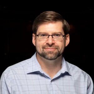 Steven Grair in a checked shirt and glasses, portrait
