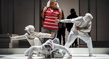 Dancers in white strike poses around a singer in a red striped shirt in Pittsburgh Opera's We Shall Not Be Moved