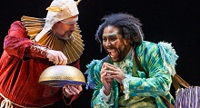 Dr. Bartolo in a spiked gold ruff offers a gold bowl to a laughing woman in green in Pittsburgh Opera's Ariodante