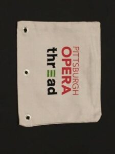 A white canvas pencil case printed with the Pittsburgh Opera and Thread logos
