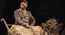 A grinning young man in a flat cap sits in a wagon beside a tangle of wire in Pittsburgh Opera's Proving Up