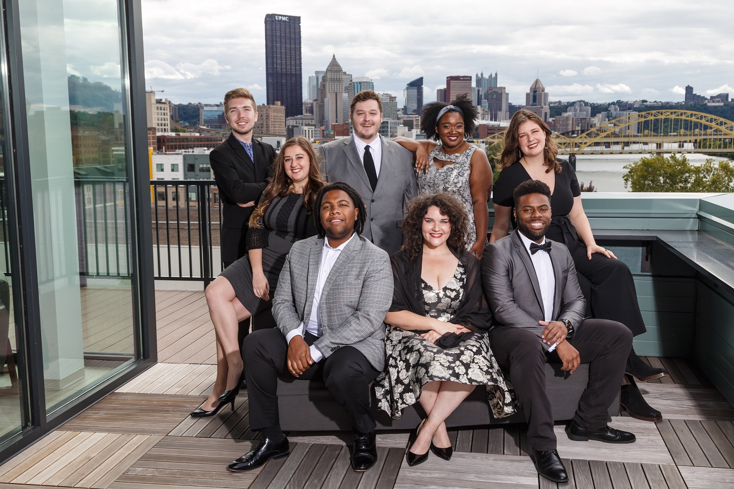 The 2022-23 Pittsburgh Opera Resident Artists pose on a rooftop deck with the Downtown Pittsburgh skyline behind them