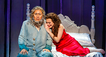 Rusalka in a red gown leans on Vodnik in a blue robe on a white bed in Pittsburgh Opera's Rusalka