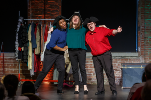 Three Resident Artists in pirate hats sing arm in arm before a costume rack at a Song Shop concert