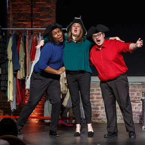 Three Resident Artists in pirate hats sing arm in arm before a costume rack at a Song Shop concert