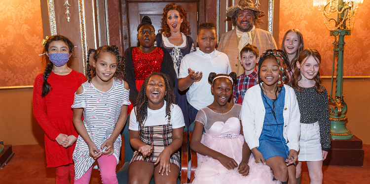 Students pose with two costumed cast members in a gilded lobby after a Barber of Seville student matinee