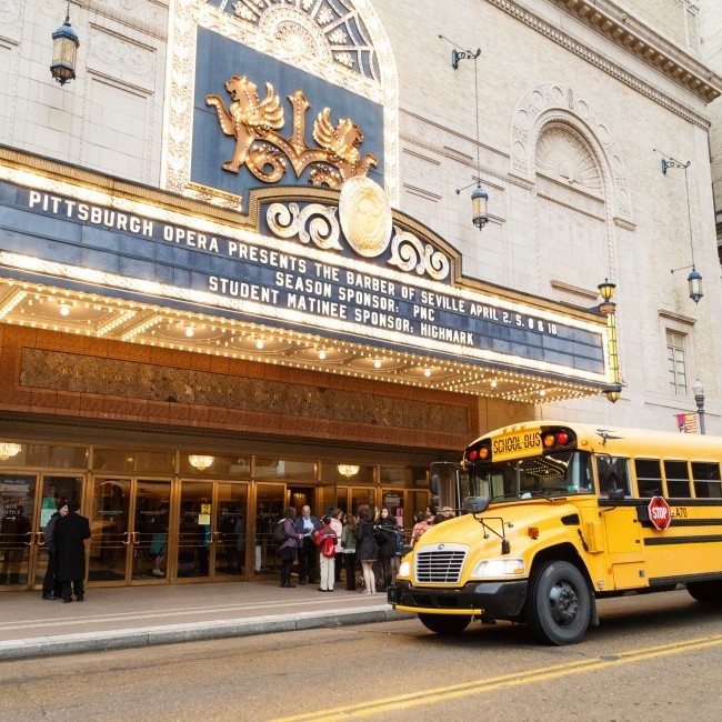 A yellow school bus pulls up under the Benedum Center marquee for a Pittsburgh Opera student matinee