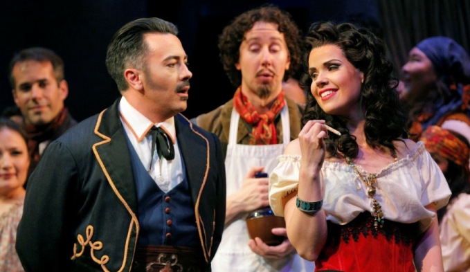 Carmen in a peasant blouse toys with a stick beside Don Jose in a braided uniform jacket in Pittsburgh Opera's Carmen