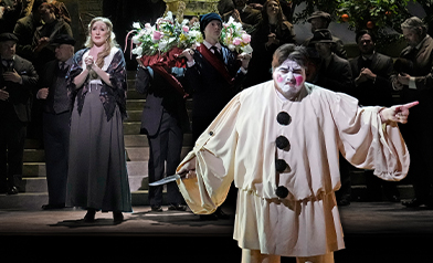 Nedda in a lace shawl clasps her hands as Canio in a white clown costume gestures in Pittsburgh Opera's Pagliacci