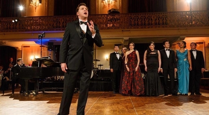 A tenor in a tuxedo sings before Resident Artists in gowns and black tie in a gilded ballroom at the Diamond Horseshoe Ball