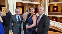 Emily Richter in a navy gown poses with three guests in the Metropolitan Opera House lobby