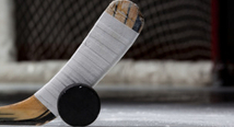 A taped hockey stick blade rests against a puck on the ice