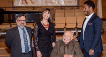 Three Pittsburgh Opera staff and singers pose with a seated James Benner in a recital hall