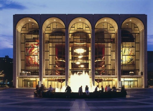 The Metropolitan Opera House facade at night with its five arched windows and lit fountain