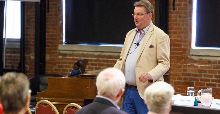 Antony Walker speaks to a seated audience beside a grand piano at a 2017 Opera Up Close at the Bitz Opera Factory