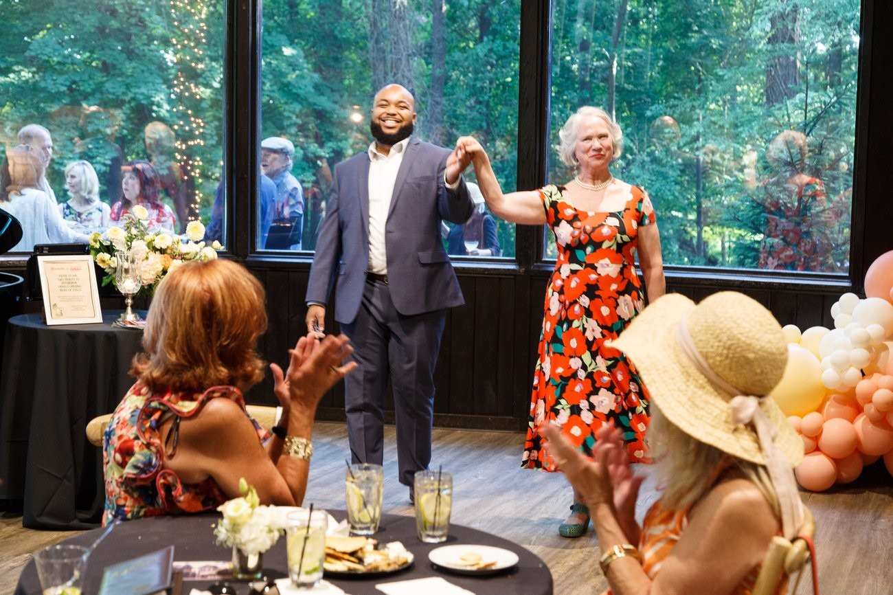 A baritone in a blue suit and a soprano in a floral dress take a bow before applauding guests at an Outside the Salon event