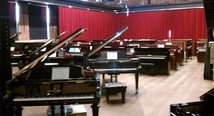 Rows of grand pianos before a red curtain at the Pittsburgh Opera piano sale