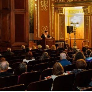 A speaker at a podium addresses a seated audience in the gilded Benedum Center