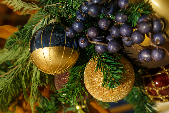 Close-up of gold and navy ornaments and blue berries on evergreen garland